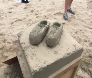 Zandsculpturen van schoenen waarbij de hakken in het zand staan. 